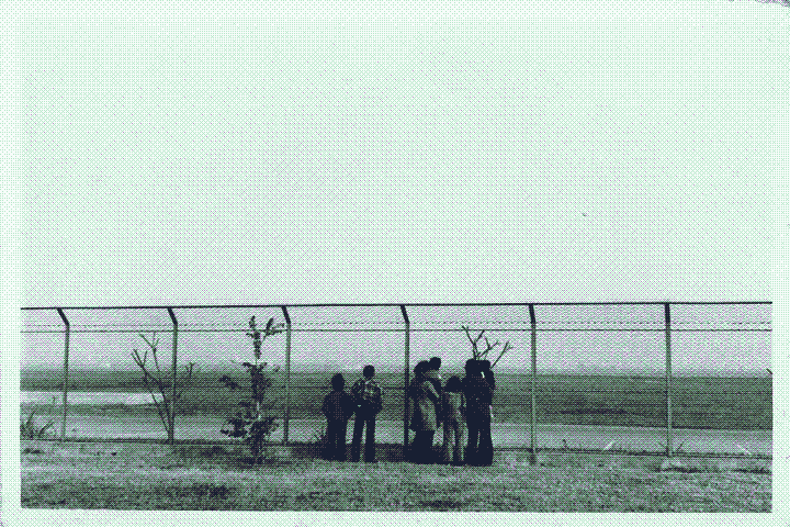 A family standing behind the gates of a tarmac, looking up at the sky